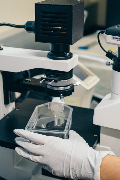 A gloved hand positioning a sample beneath a laboratory microscope