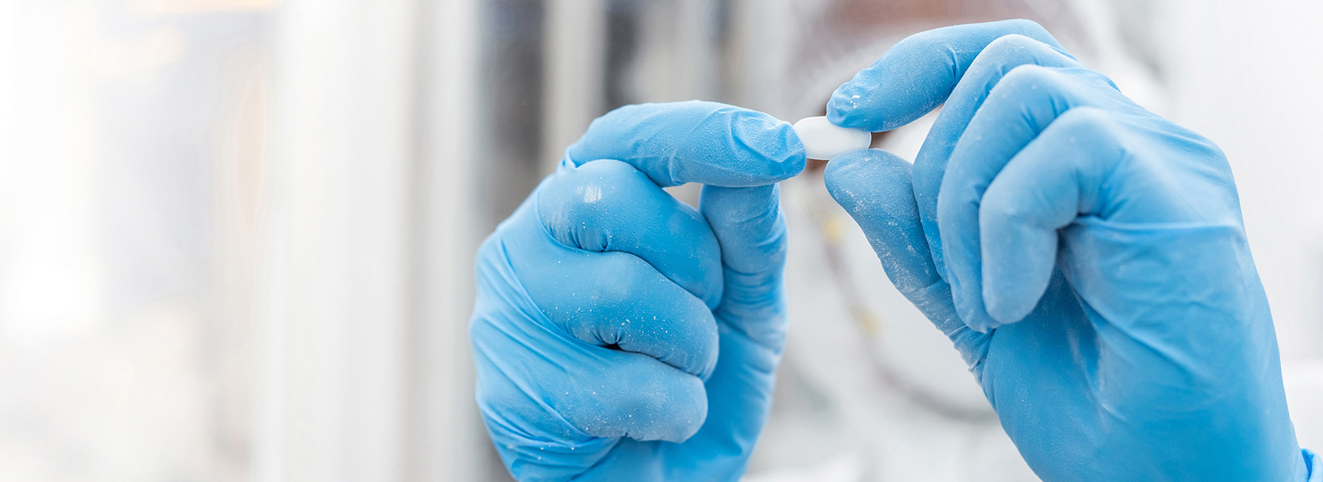 Gloved hands inspecting a finished tablet under clean conditions